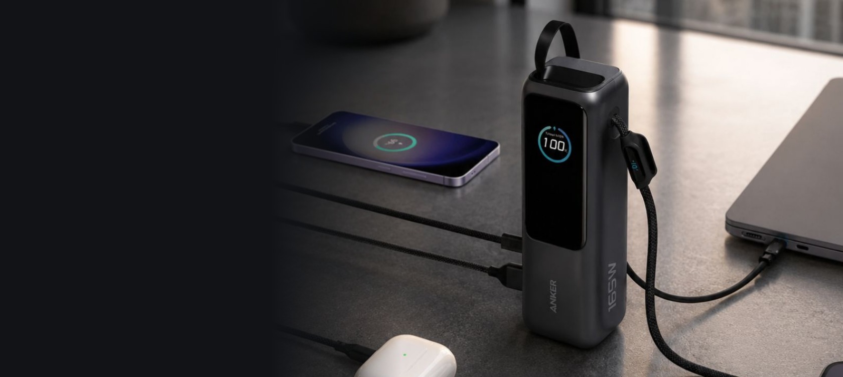 Kraftig svart Anker-powerbank lader mobil, AirPods og laptop på et mørkt skrivebord