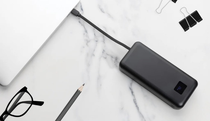 Svart powerbank med display lader en laptop på et marmorbord
