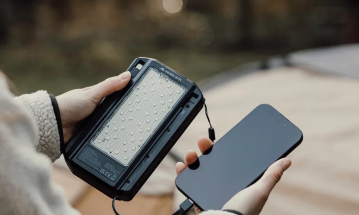 Hender holder en solcelle-powerbank med lampe ute i naturen