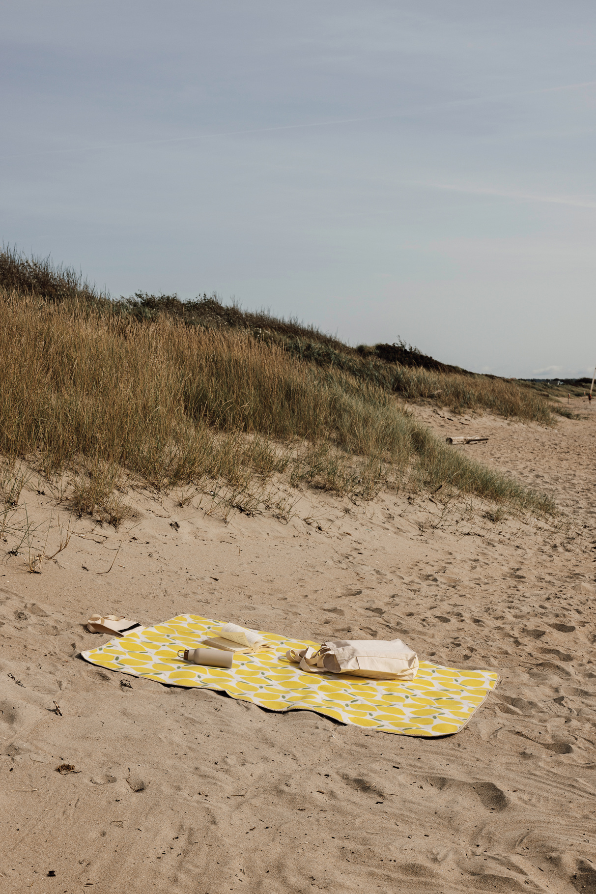 Sommergaver på stranden: gult strandhåndkle, drikkeflaske og bag i sanden