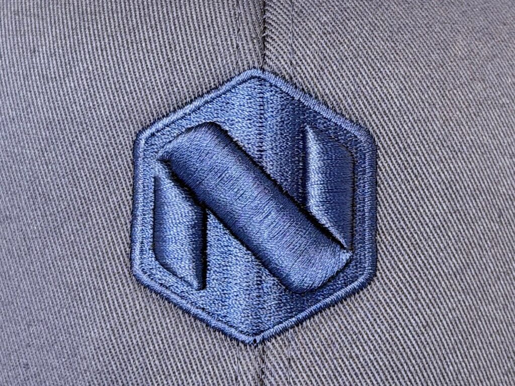 Nærbilde av brodert NorgesProfil-logo i blå tråd på mørkegrå caps