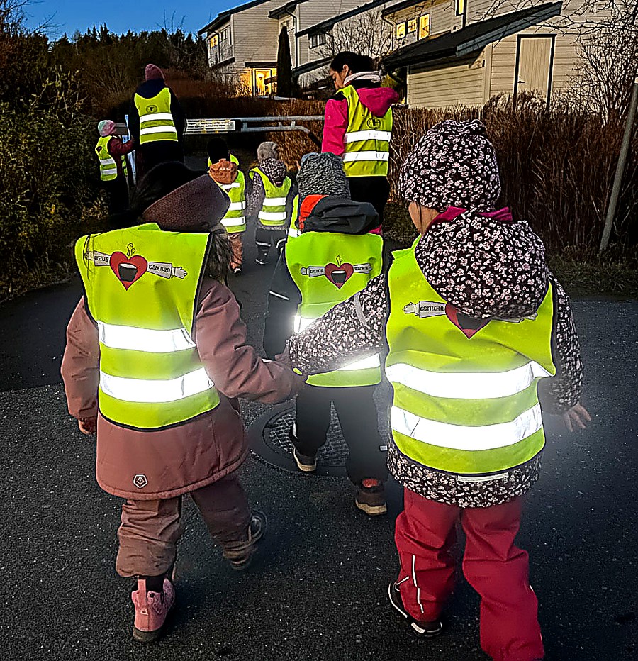 Barnehagebarn på tur i skumringen med gule refleksvester som lyser opp