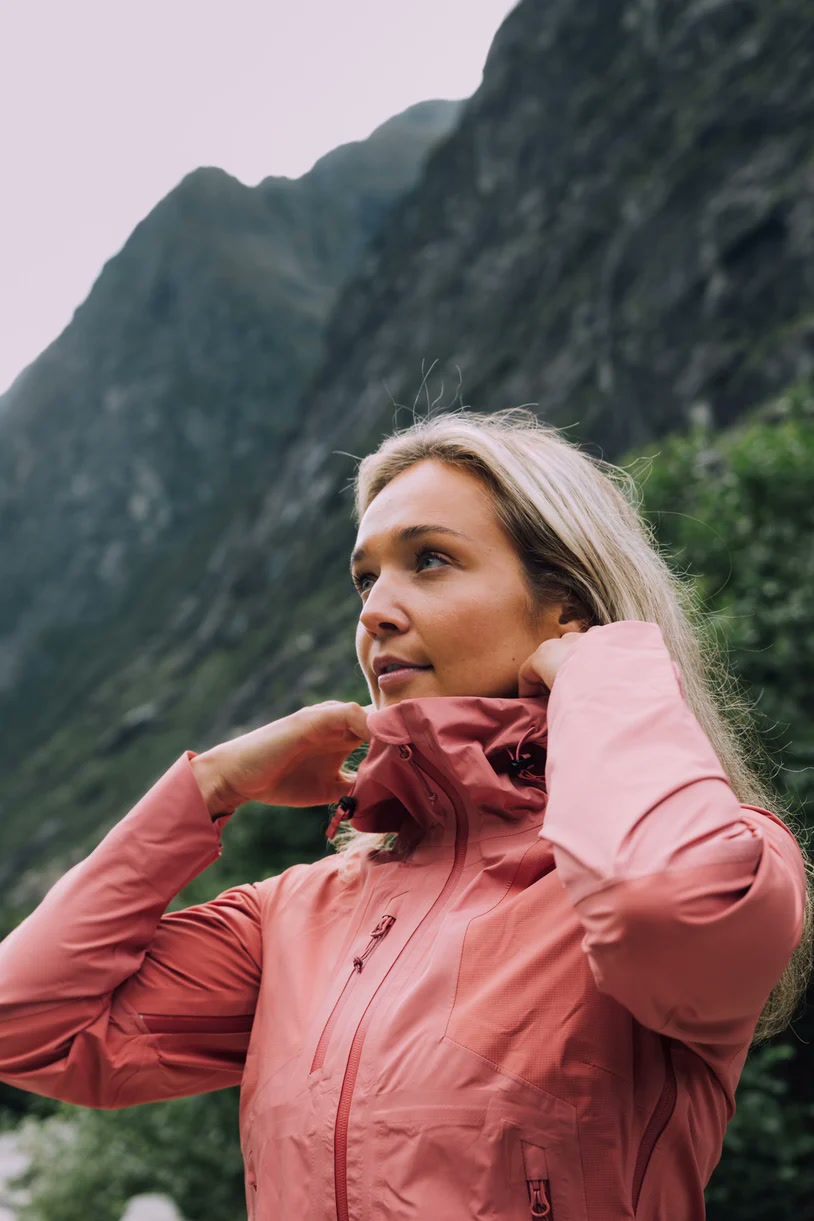 Kvinne i rosa Tufte-skalljakke foran bratte fjell